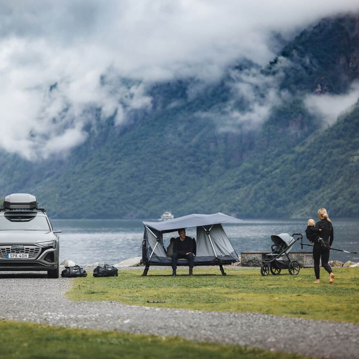 Family enjoying nature with Thule Thule Outset - 3-person towbar-mounted car tent by a lake.