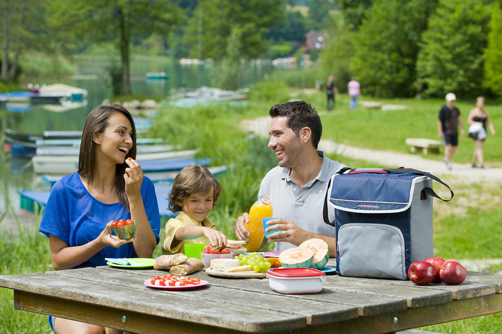 Family enjoying a picnic by the lake with Campingaz Fold'N Cool Cooler on table, keeping food fresh for outdoor adventures.