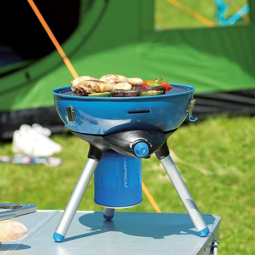 Portable camping stove with Campingaz CV470 Plus Gas Cartridge in outdoor setting, cooking food on tabletop near green tent.