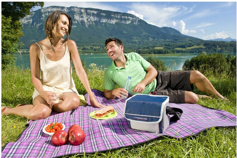 Couple enjoying a picnic with Campingaz Fold'N Cool Cooler by a scenic lake in the mountains, keeping food fresh and cool outdoors.