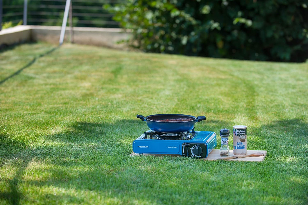 Campingaz Bistro 2 Portable Camp Stove set on grass with cooking pan and condiments in a garden setting
