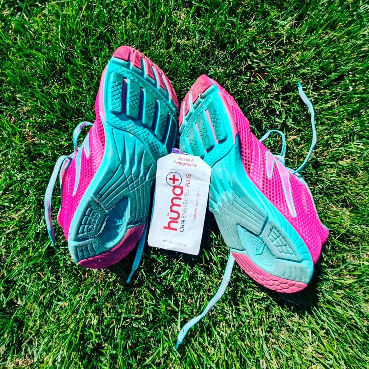 Huma Chia Energy Gel Plus - Berries & Pomegranate packet placed between colorful athletic shoes on grass