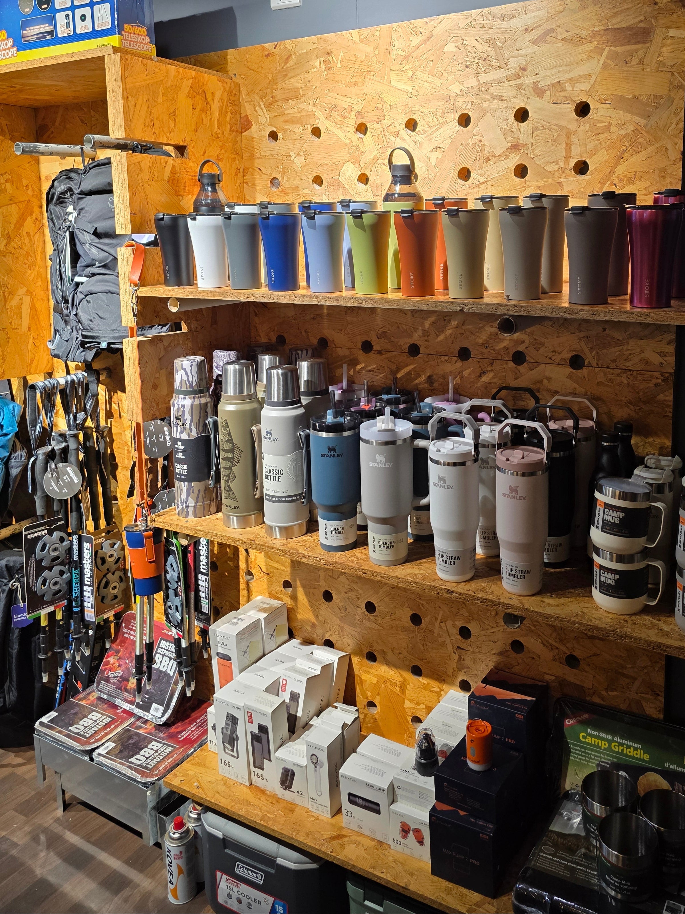 A retail display shelf filled with numerous paint cans, bottles, and tool boxes on a wooden pegboard and counter inside a store.