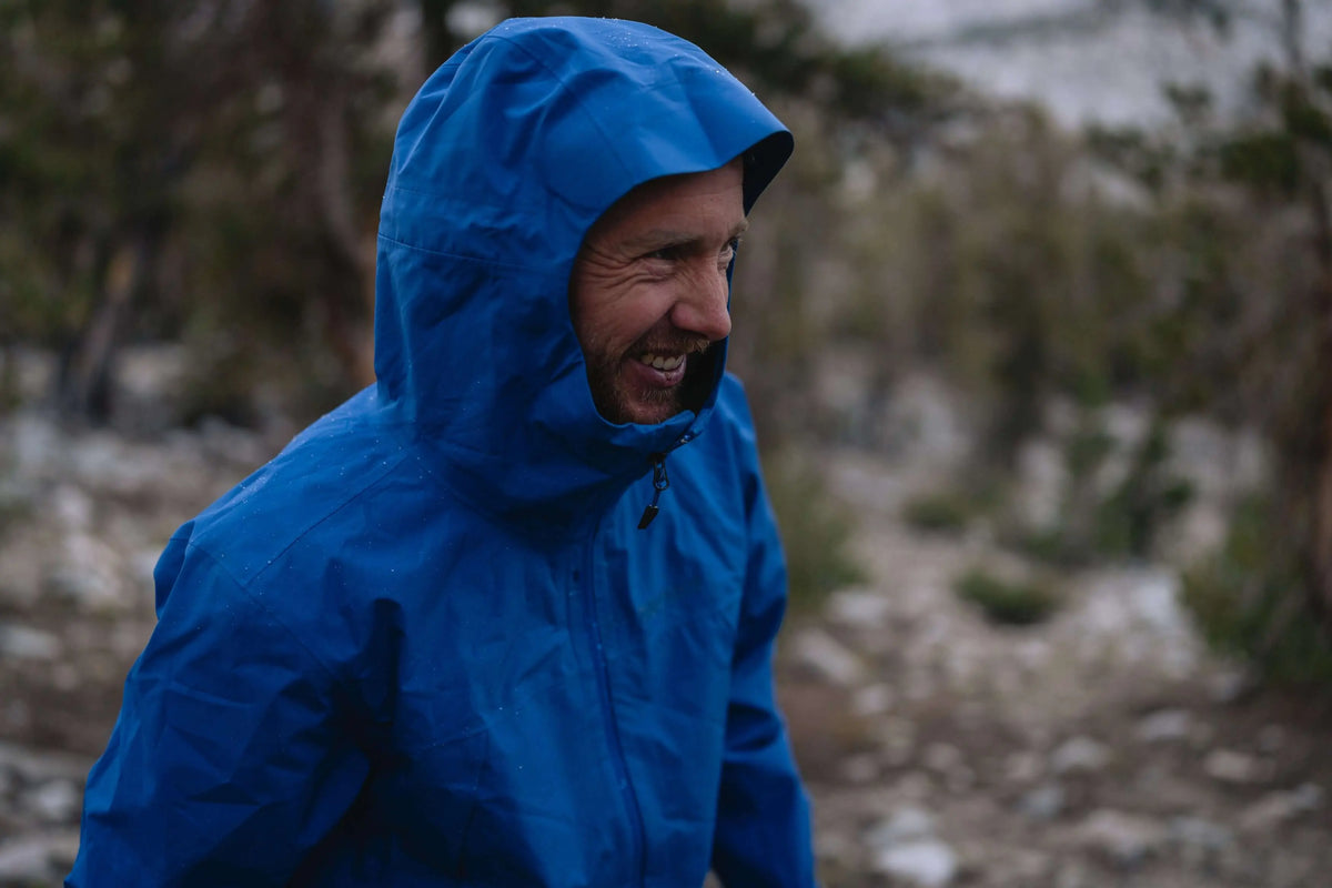 Man wearing Marmot Gore-Tex Minimalist Pro Jacket in blue, enjoying a hike in nature.