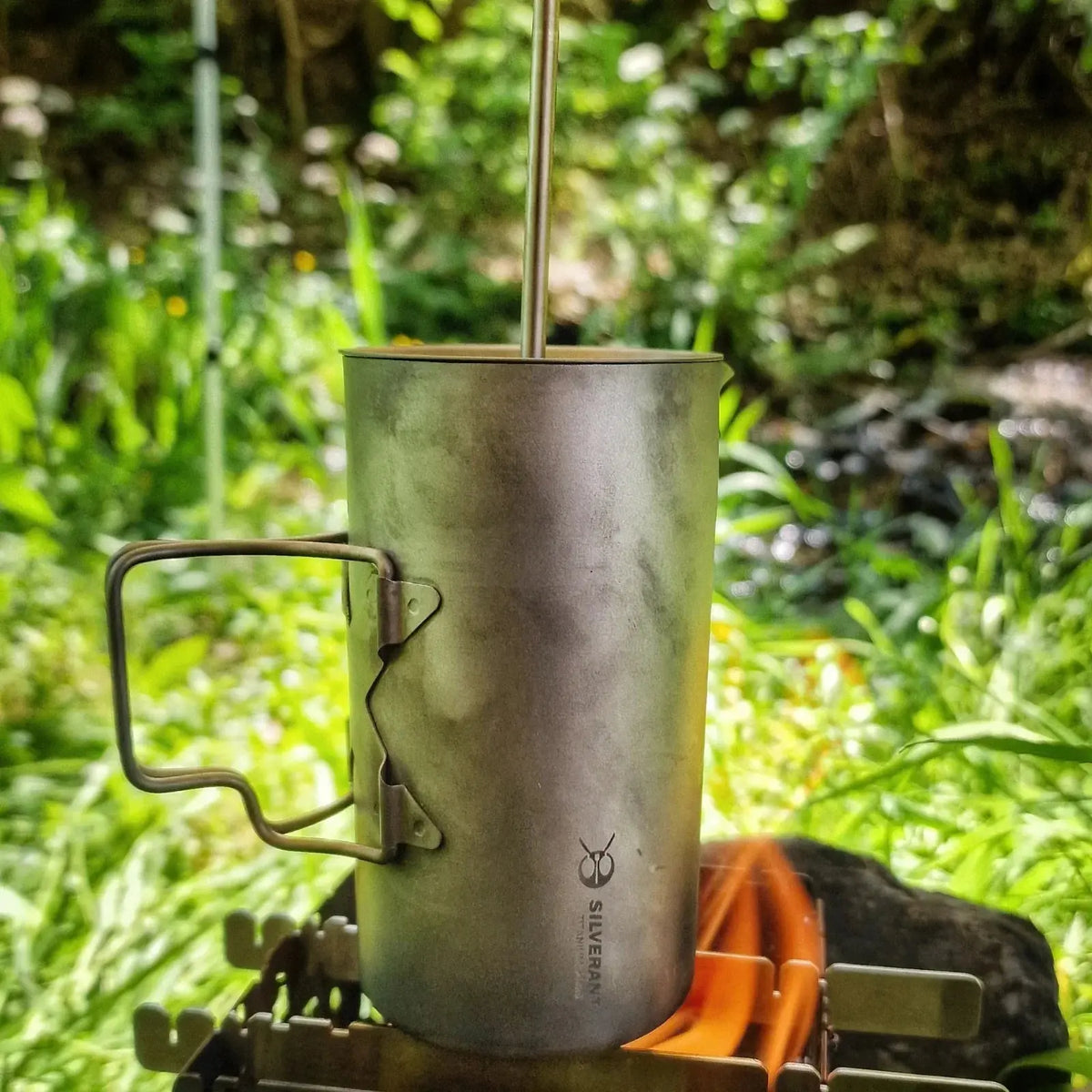 SilverAnt Ultralight Titanium Coffee French Press outdoors with foliage background, 17 oz capacity showcasing its durability and style.