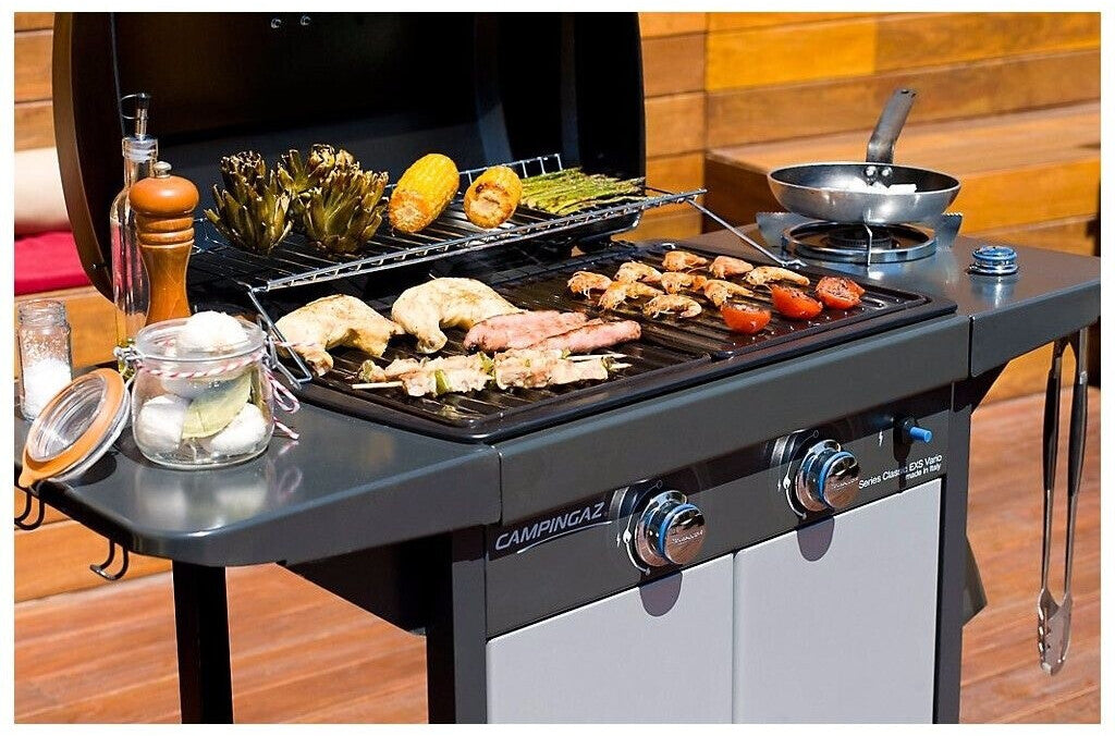 Campingaz 2 Series EXS Vario D Gas Grill with assorted grilled food on the cooking surface in an outdoor setting.