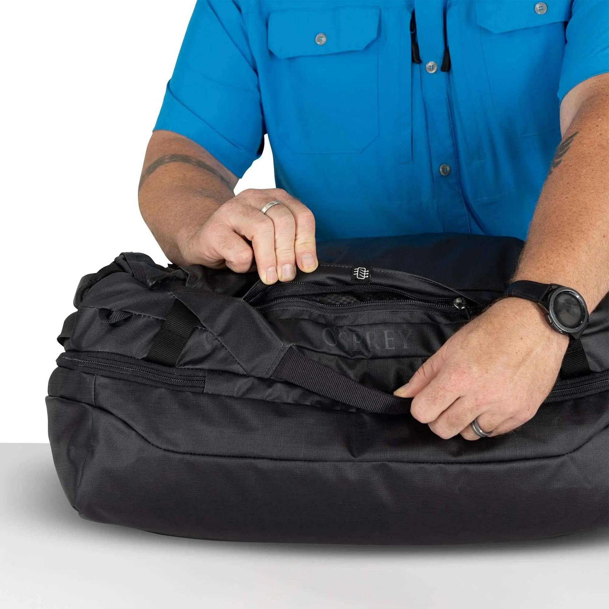 A person adjusting the strap of the Transporter Squffel 44 bag, showcasing its rugged design and functionality.