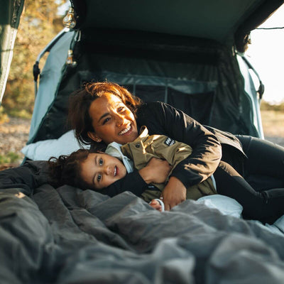 Mother and child relax in Thule Thule Outset - 3-person towbar-mounted car tent, showcasing camping comfort and convenience.