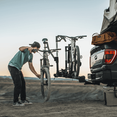Cyclist using Thule Verse Bike Repair Holder for trailhead adjustments with Thule bike rack on a truck
