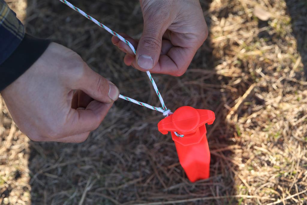 Placing Coghlan's Ground Spike into the ground for securing a tent, highlighting its high visibility and heavy holding power.