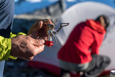 Person holding MSR PocketRocket 2 Stove with campsite in background, showcasing lightweight camping gear for outdoor adventures.