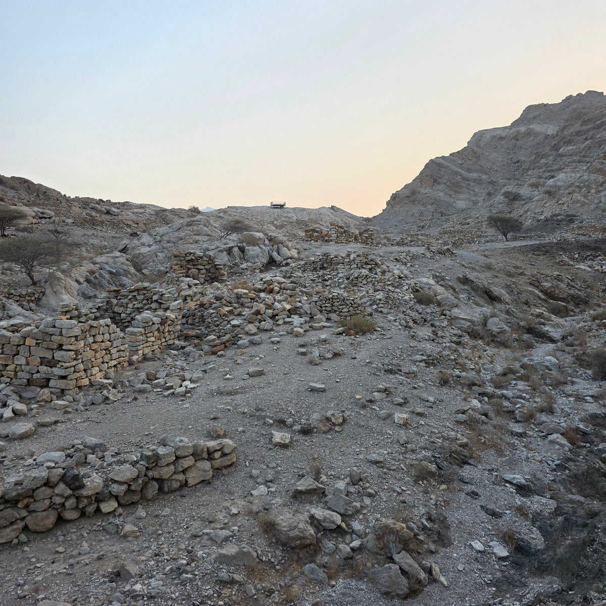 A rocky desert landscape with stone ruins in the foreground, a pale sky, and a sunlit hillside on the right.