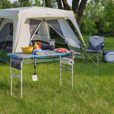 Core Equipment 4 Foot Outdoor Table with FlexRail — backyard tailgate scene with grill and cooler.