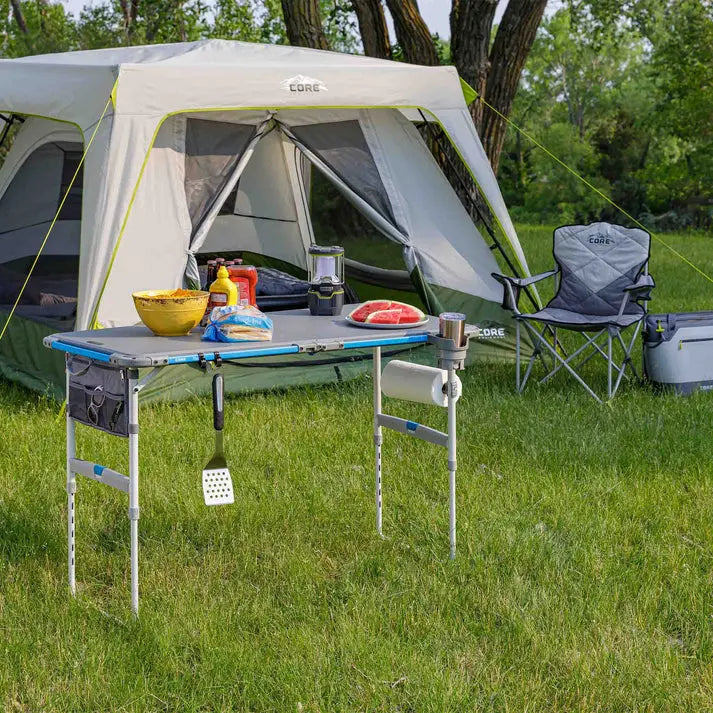 Core Equipment 4 Foot Outdoor Table with FlexRail — backyard tailgate scene with grill and cooler.
