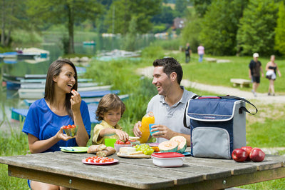 Family enjoying a picnic by the lake with Campingaz Fold'N Cool Cooler on table, keeping food fresh for outdoor adventures.
