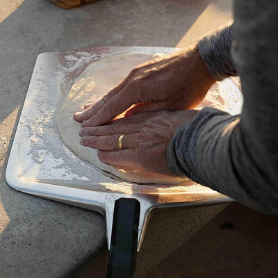 Person preparing pizza dough on an Ooni Pizza Peel for outdoor cooking.