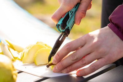 Person using Leatherman Signal multi-tool to slice fruit outdoors.
