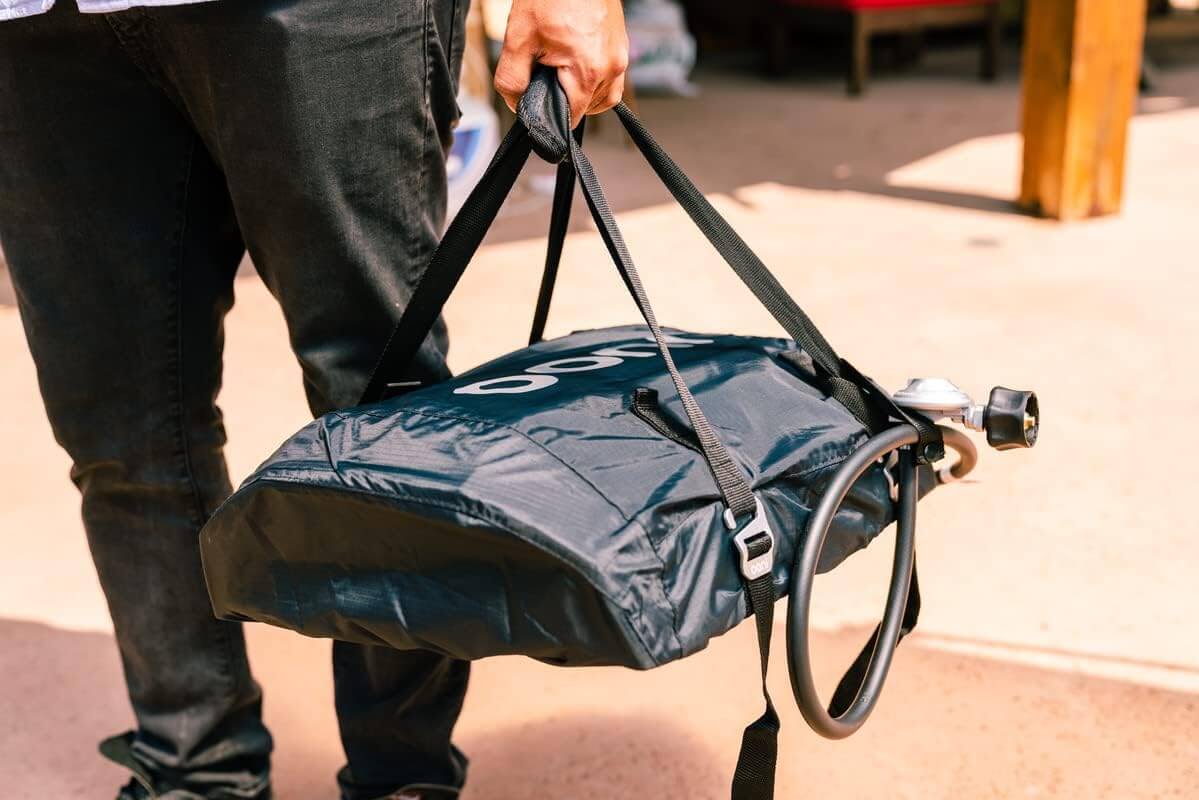 Person carrying Ooni Carry Cover for Ooni Koda 12, showcasing portability and protection for outdoor cooking appliances.