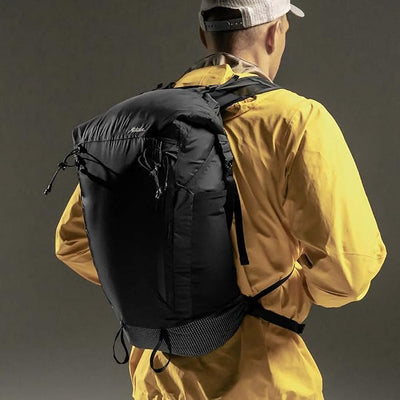Person wearing a black backpack and yellow jacket on a dark background