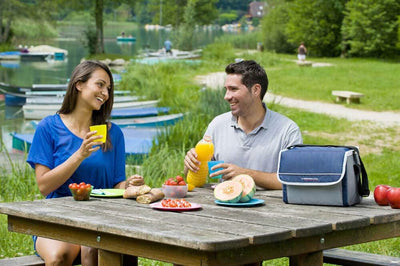 Couple enjoying a picnic by the lake with Campingaz Fold'N Cool Cooler, showcasing outdoor food and beverage storage.