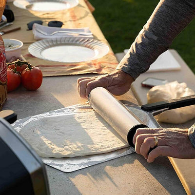 Outdoor pizza preparation using Ooni Pizza Peel and rolling pin on a sunny day.