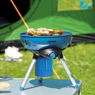 Portable camping stove with Campingaz CV470 Plus Gas Cartridge in outdoor setting, cooking food on tabletop near green tent.