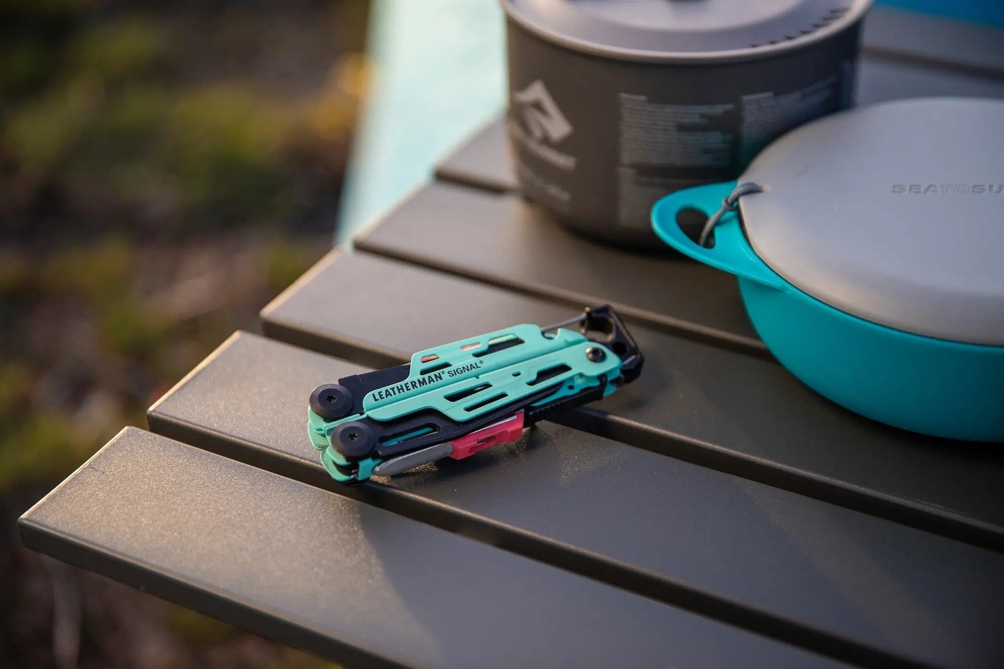 Leatherman Signal Multi-Tool in green on outdoor table next to camping cookware, ideal for survival and adventure in UAE terrains.