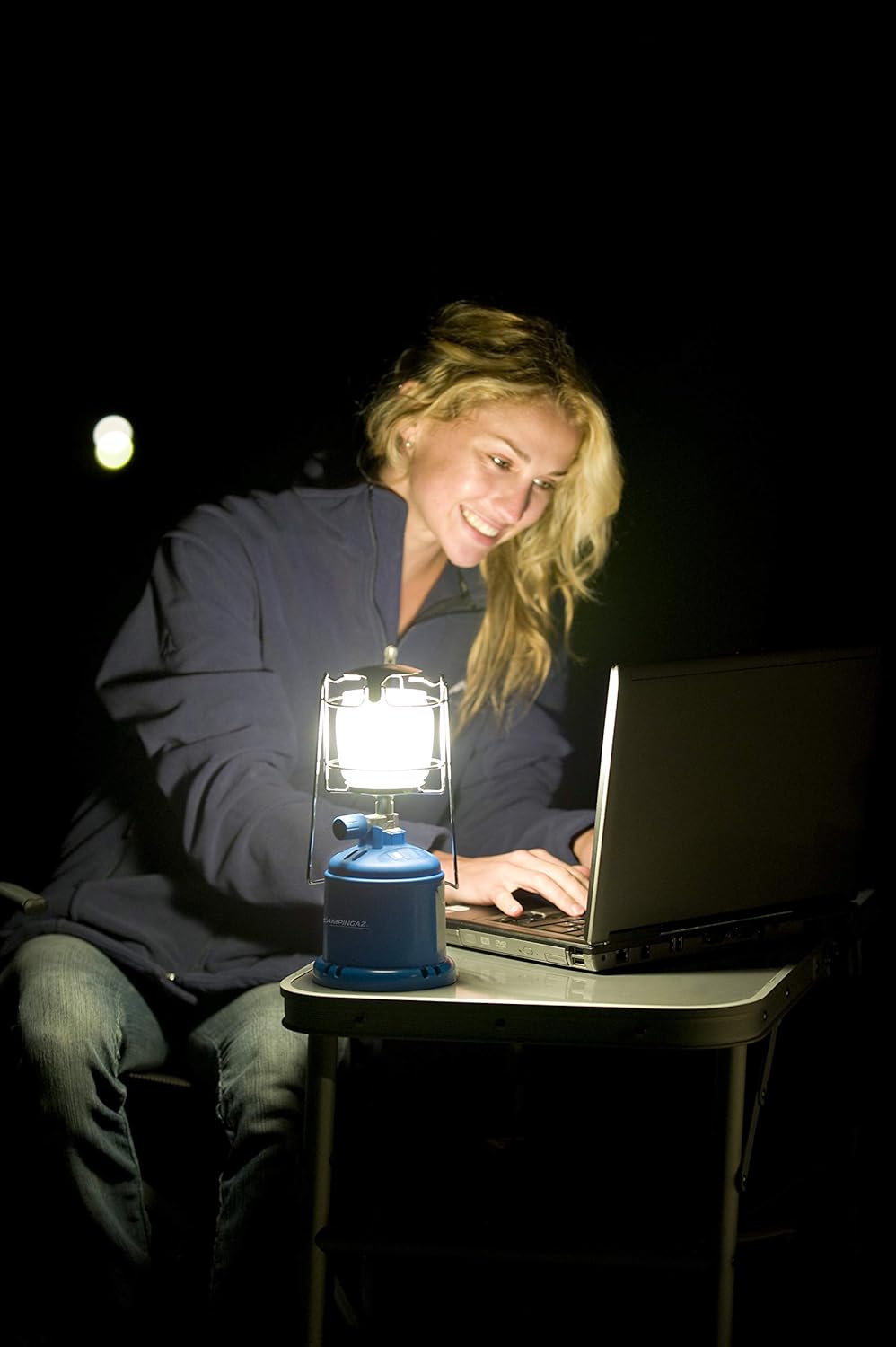 Woman camping at night using a laptop illuminated by Campingaz 206L Gas Lantern