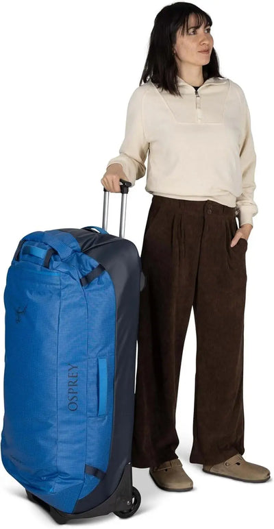 Transporter Wheeled Duffel 120 by Osprey; a woman standing with a blue wheeled duffel bag.