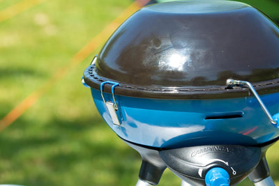 Close-up of Campingaz Party Grill 400 with blue lid in outdoor setting, perfect for camping and outdoor cooking adventures.