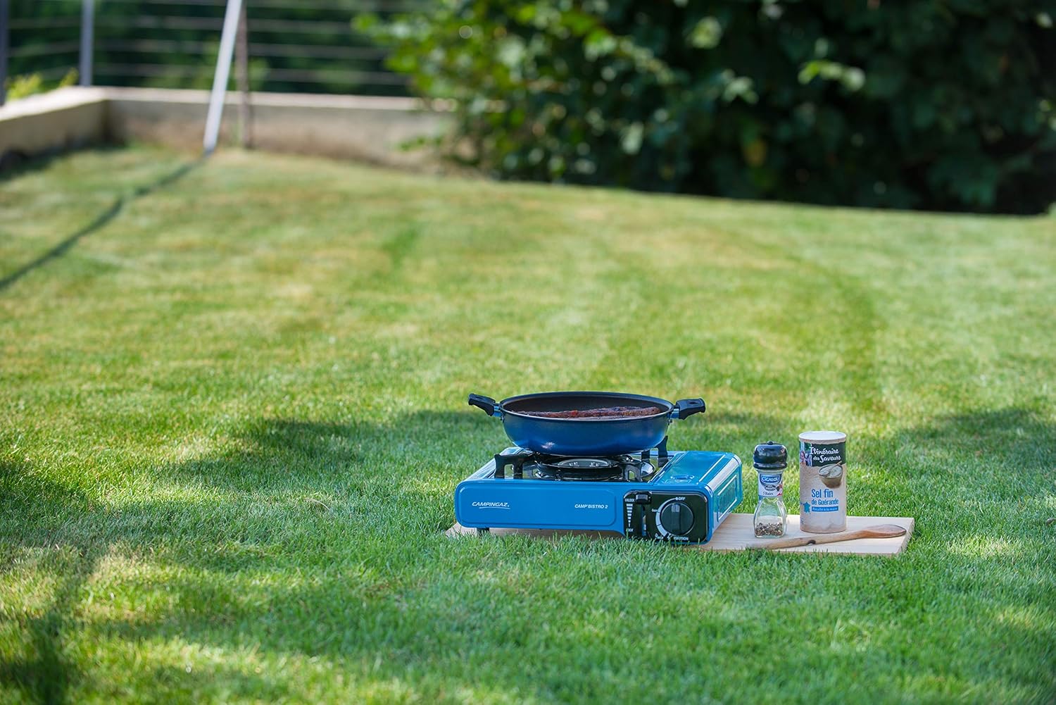 Campingaz Bistro 2 Portable Camp Stove set on grass with cooking pan and condiments in a garden setting