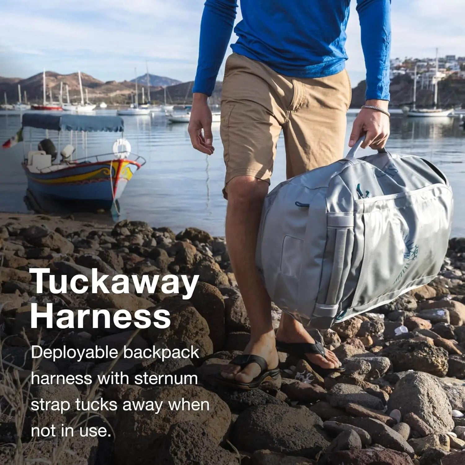 Osprey Transporter Duffel 120 with stowaway harness on rocky shore, weather-resistant travel gear.