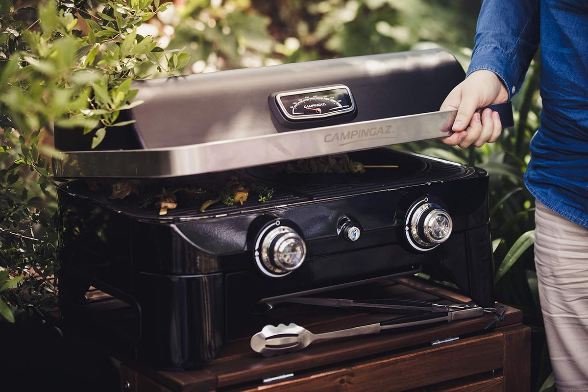 Person using Campingaz Attitude 2100 LX Portable Gas Grill on outdoor patio setup.