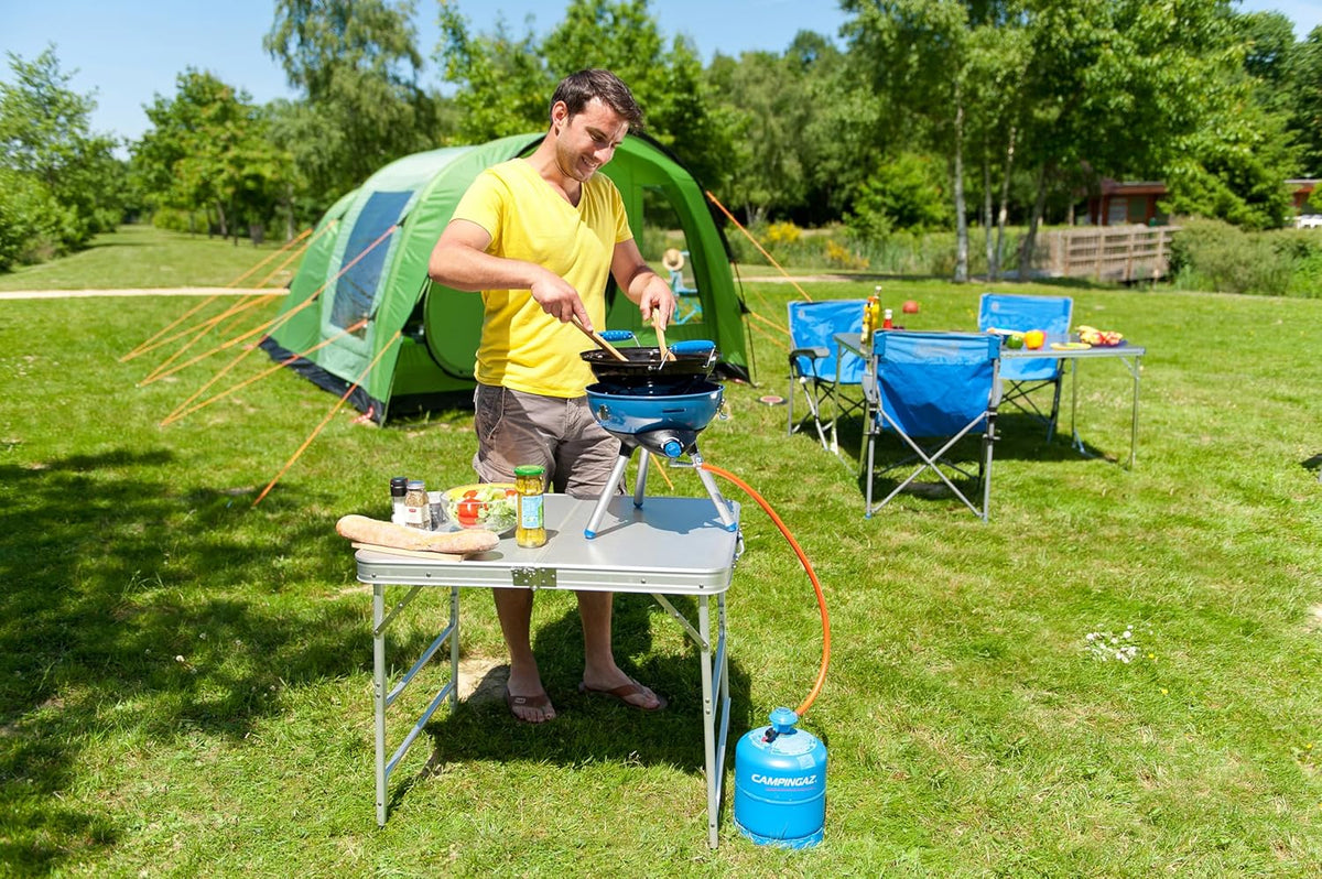 Man using Campingaz Party Grill 400 at campsite, surrounded by tent and camping chairs