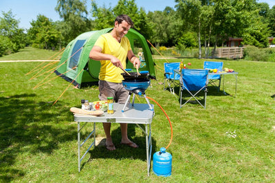 Man using Campingaz Party Grill 400 at campsite, surrounded by tent and camping chairs