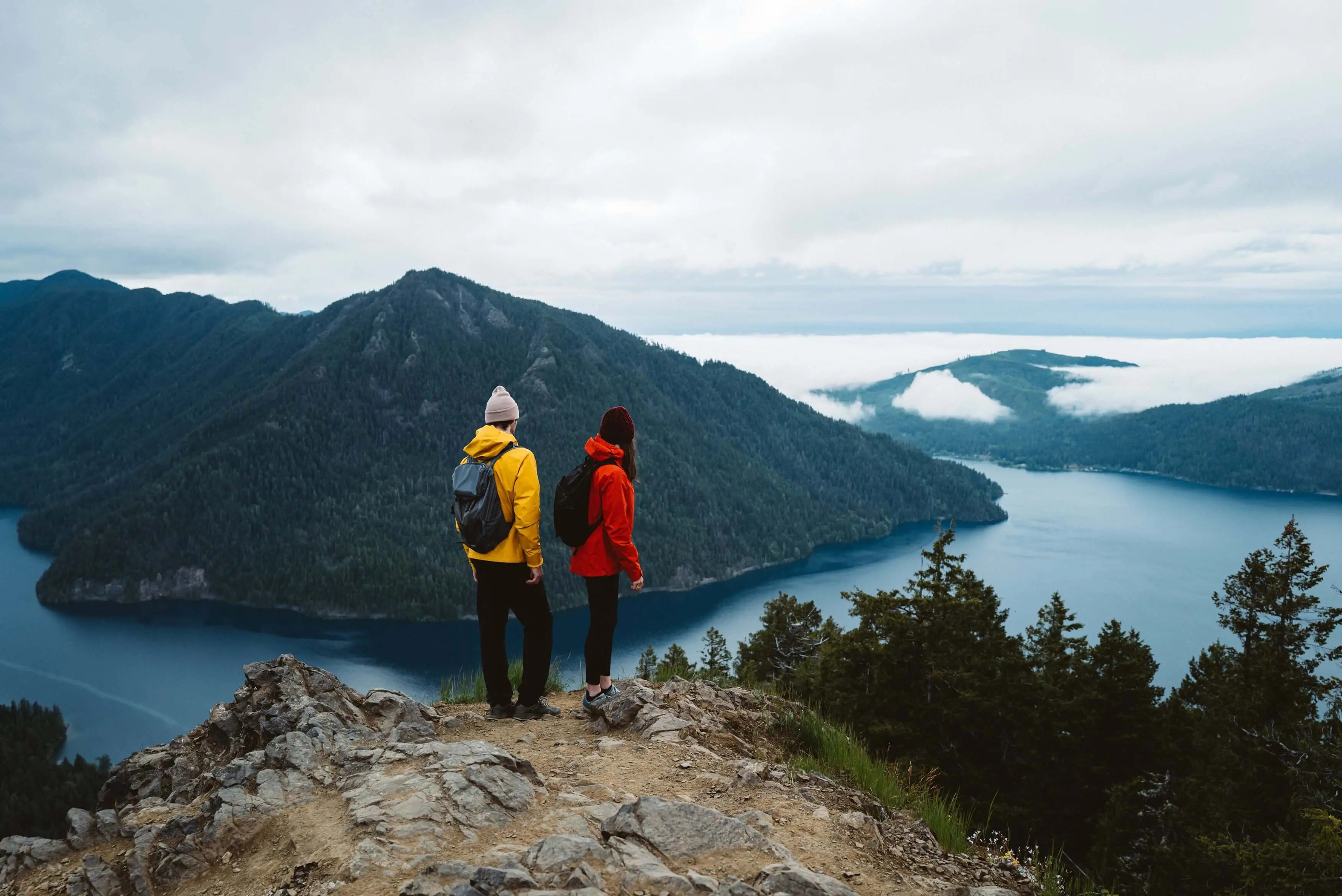 Hikers overlooking a mountain lake, wearing vibrant jackets for outdoor exploration, exemplifying the Marmot Gore-Tex Minimalist Pro Jacket.