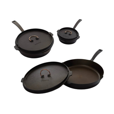 A set of three black cast iron skillets of different sizes with copper accents and lids, displayed against a white background.
