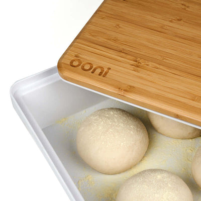 Ooni Pizza Prep Lid bamboo board on white tray with dough balls, showcasing its moisture-resistant surface for pizza preparation.