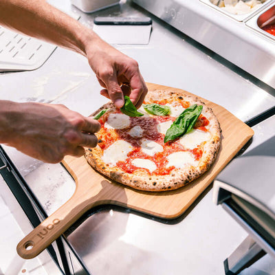 Ooni Bamboo Pizza Peel and Serving Board holding a freshly baked wood-fired pizza