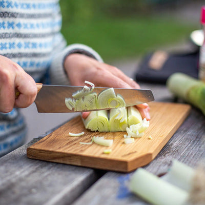 Slicing vegetables with Primus CampFire Cutting Set knife and board at a campsite.