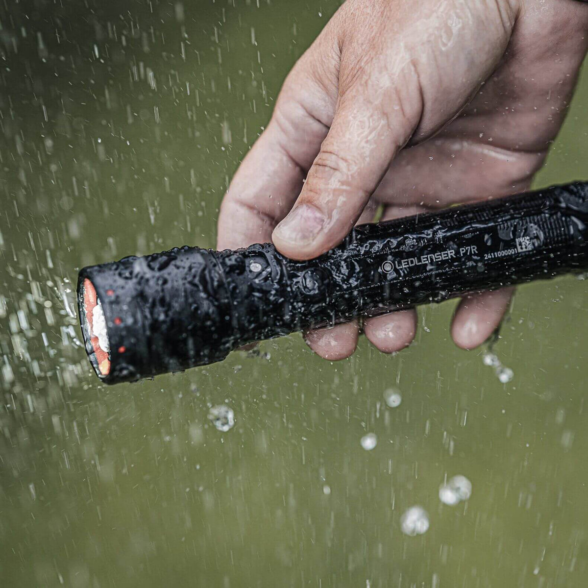 Hand holding a P7R flashlight, showcasing its waterproof feature with water droplets splashing around.
