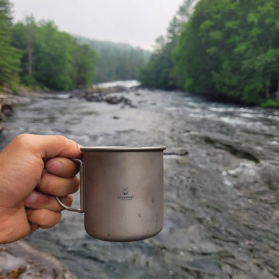 SilverAnt Ultralight Titanium Cup with Lid held by river, perfect for outdoor adventures in UAE.