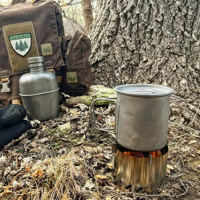 SilverAnt Ultralight Titanium Cup with Lid on a camping trip in the forest, beside backpack and canteen