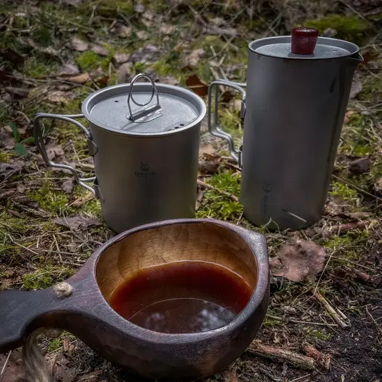 Outdoor scene featuring SilverAnt Ultralight Titanium Cup with Lid, essential gear for UAE adventures, next to a wooden cup.