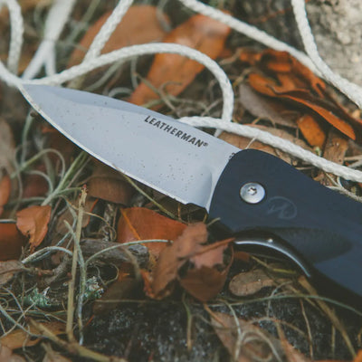 Leatherman C33 folding pocket knife on leaves with rope, perfect for outdoor adventurers.