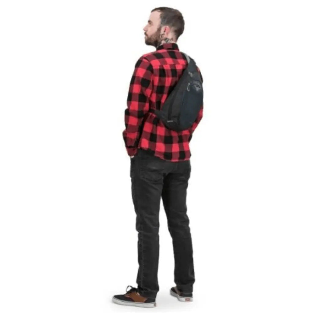 Man wearing Osprey Daylite Sling with red plaid shirt, showcasing the ambidextrous carry and sleek design.