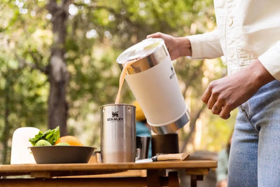 Classic Stay Chill Beer Pitcher - 64 oz / 1.9 L pouring beverage into a stainless steel cup outdoors.