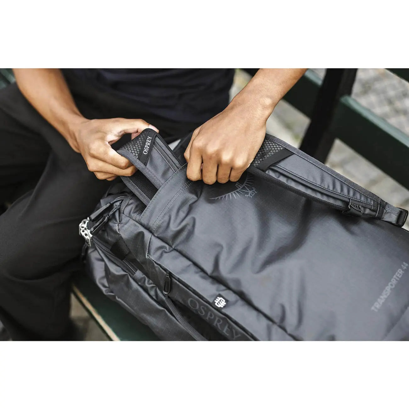 User adjusting the straps of the Osprey Transporter Squffel 44 travel bag on a bench.