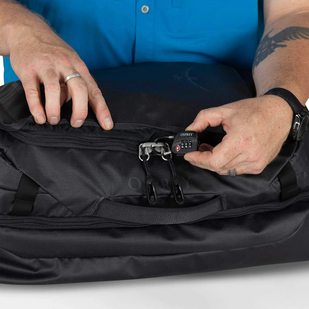 Close-up of hands using the lock on the Osprey Transporter Squffel 44 travel bag, showcasing its durable design.