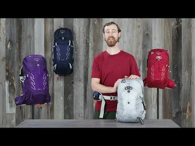 A person showcasing the Talon Jr - Kids backpack, available in multiple colors on a wooden backdrop.